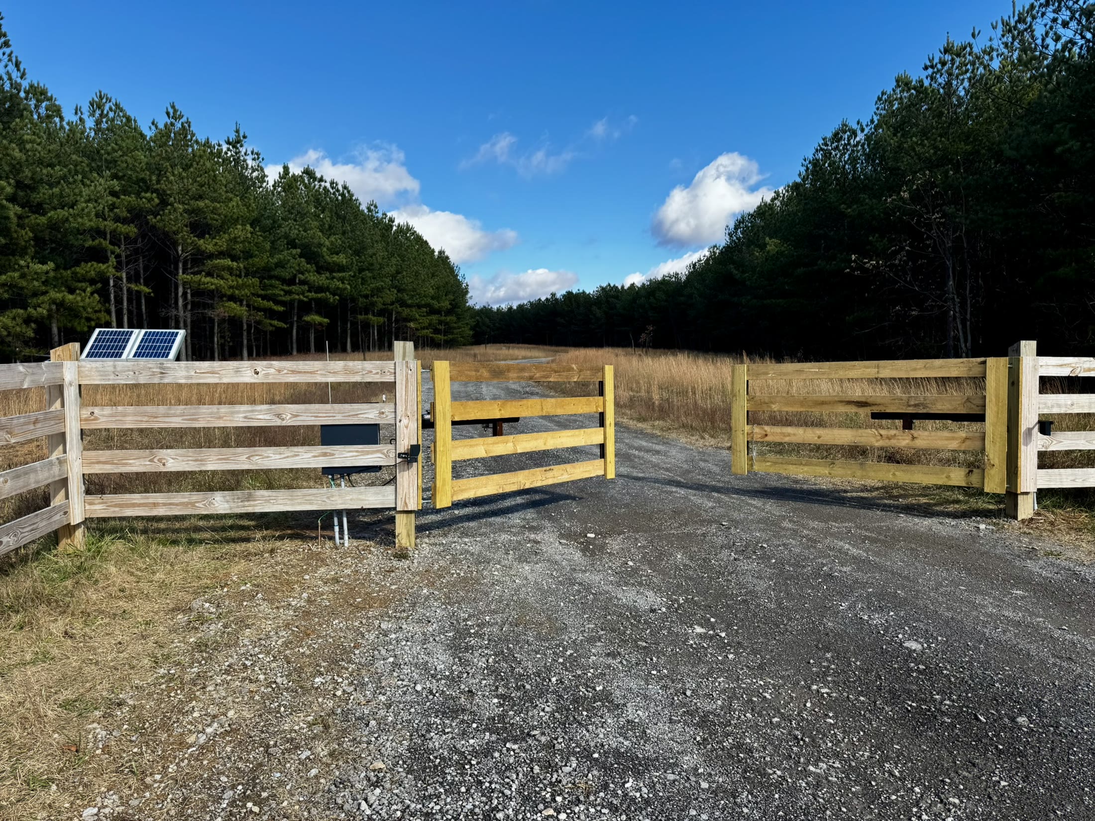 Solar-powered wooden driveway gate opening onto a gravel drive through North Georgia pines
